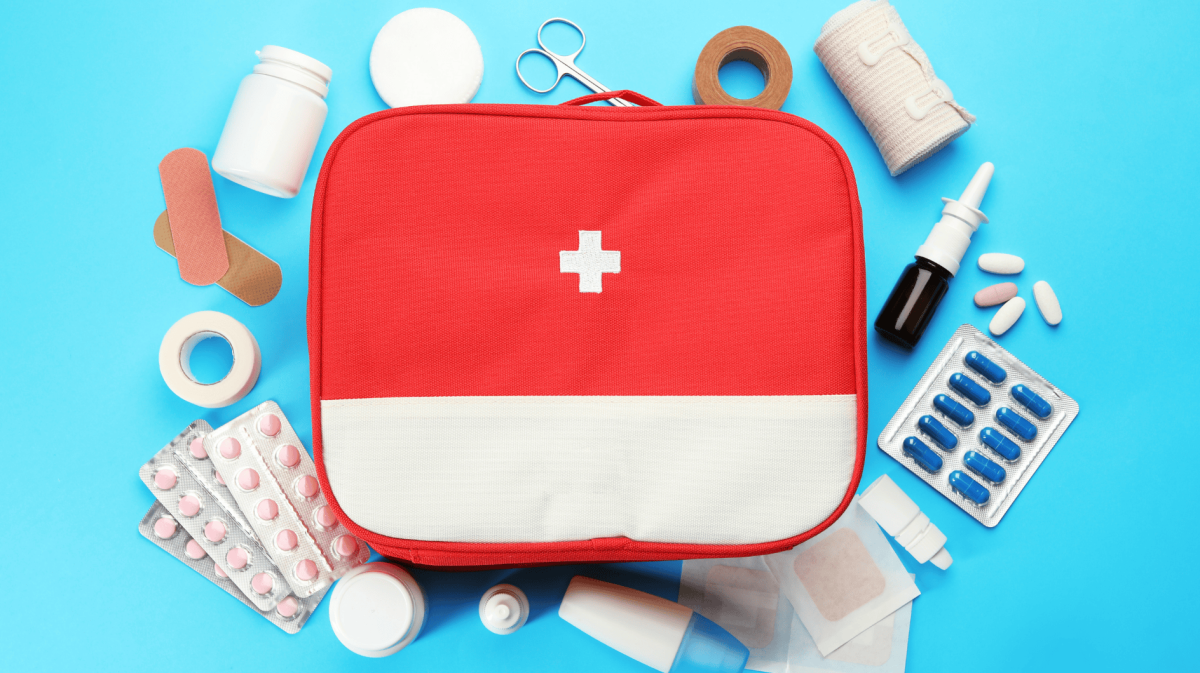 Medizinkästchen auf blauem Untergrund, darum liegen Tabletten, Mullbinden etc.