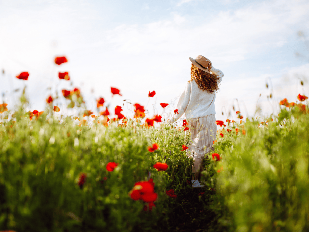 Frau mit roten Haaren l&auml;uft durch ein Feld mit Klatschmohn.