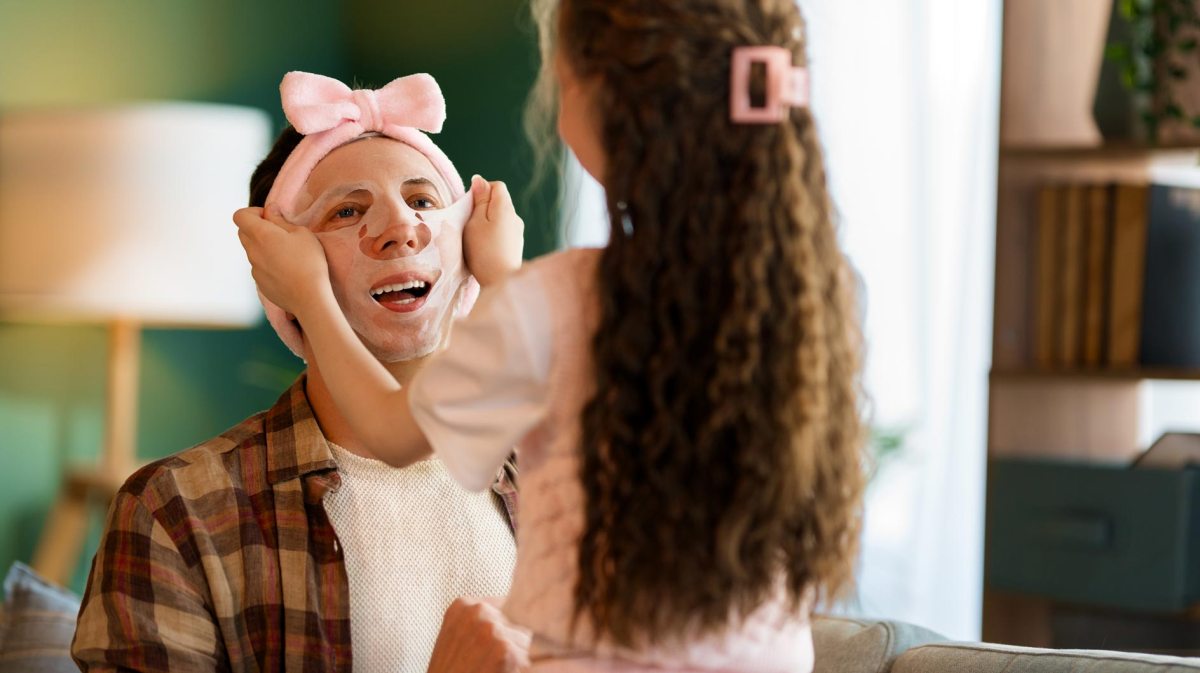 Kleine Tochter zieht ihrem Vater eine Gesichtsmaske auf.