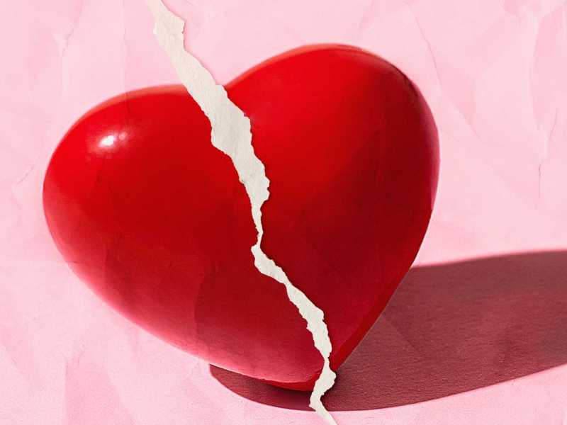 Rotes gebrochenes Herz auf pastellrosa Farbe mit zerrissenem Papiereffekt.