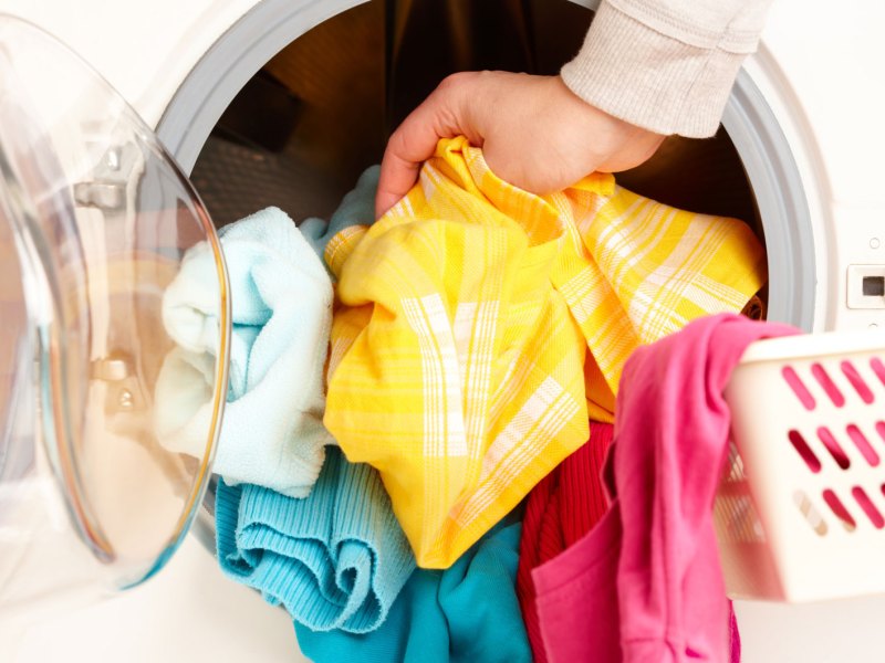 Hand legt bunte Wäsche in Waschmaschine