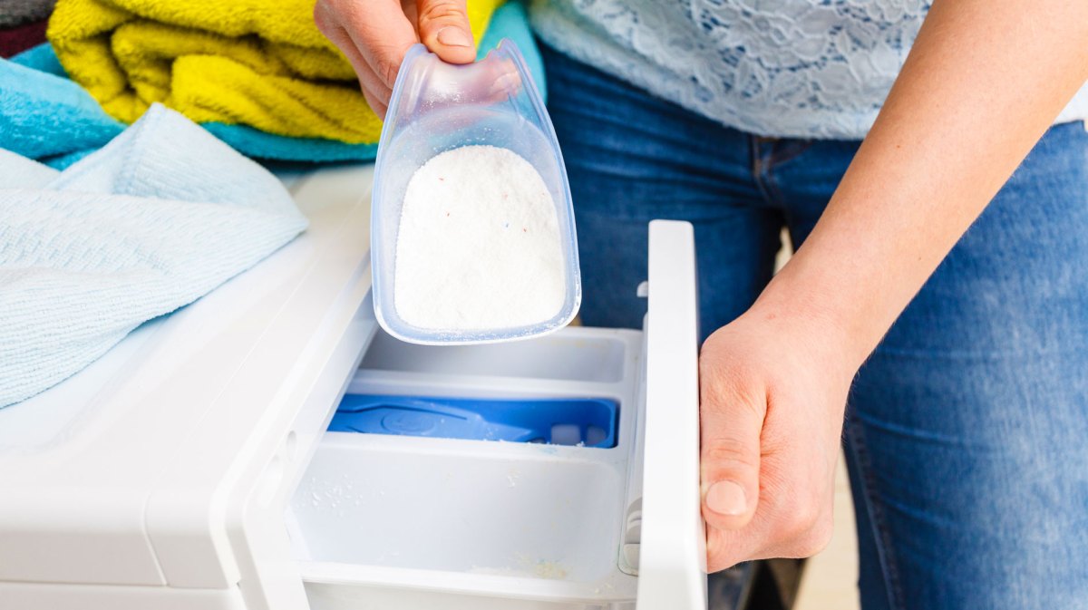 Frau füllt Waschpulver in Waschmaschine