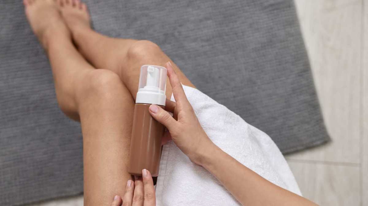 Frau hält eine Flasche Selbstbräuner über ihre Beine