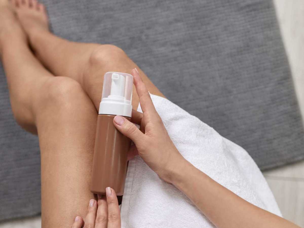 Frau hält eine Flasche Selbstbräuner über ihre Beine