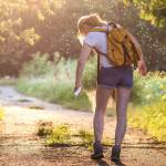 Frau auf einem Waldweg im Sommer, die sich mit Insektenschutz einsprüht.
