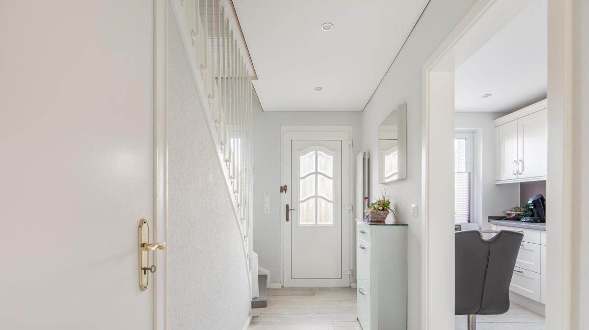 Foto eines Hausflurs mit einer weißen Haustüre und einer weißen Treppe und einem weißen Schmalen Schuhschrank.