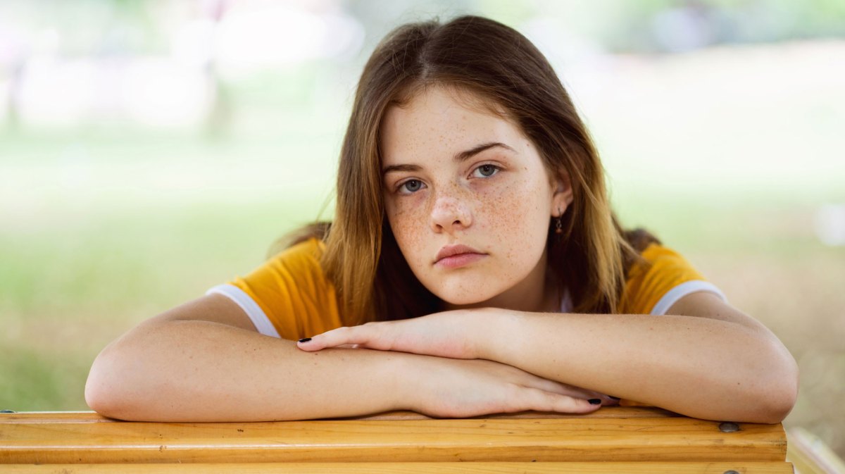 Mädchen im Teenageralter lehnt gelangweilt auf einem Tisch draußen.