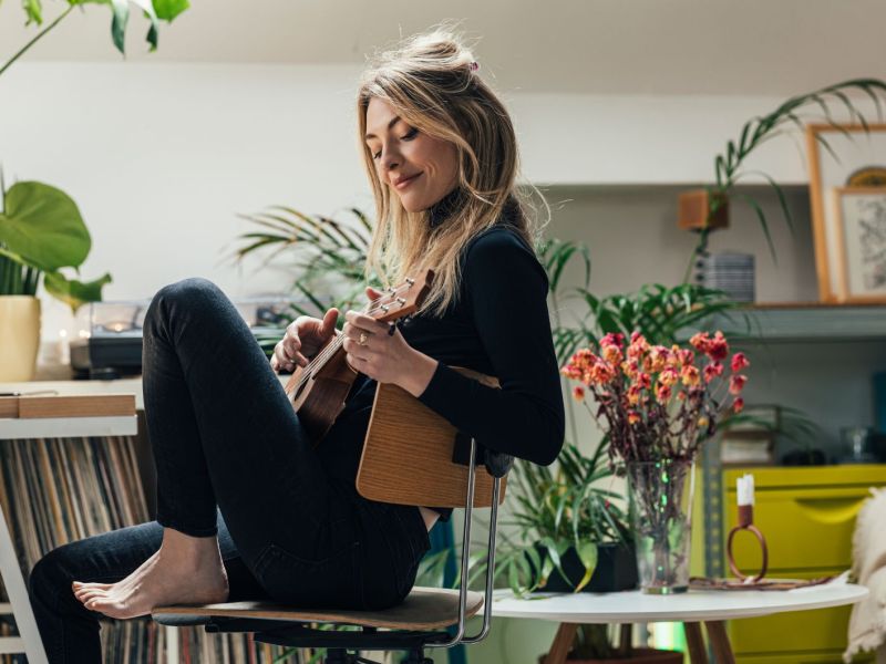 Frau spielt Ukulele in üppig dekorierter Wohnung