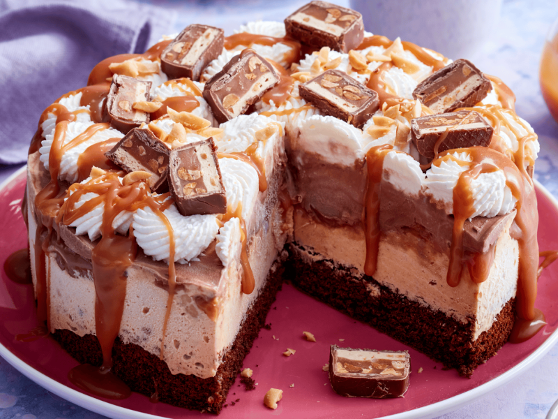 Eistorte mit Karamell und Erdnussriegeln auf einem roten Teller.