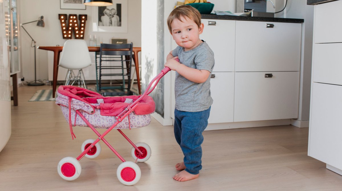 Kleiner Junge spielt mit Puppenwagen in der Küche.