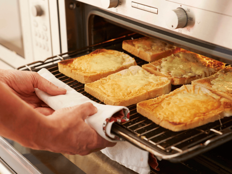 Person holt überbackenene Toastscheiben aus Ofen.