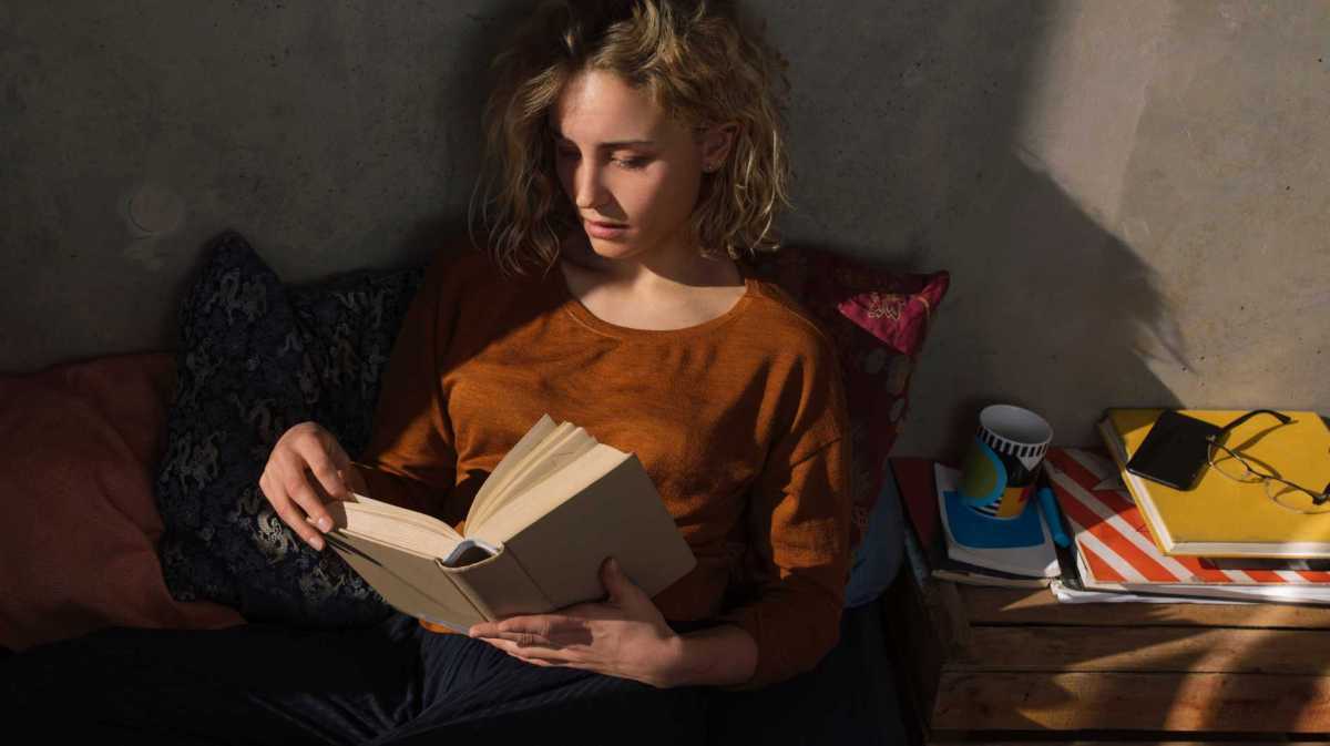 Blonde Frau liest einen Thriller im Freien. Dunkle Atmosphäre.