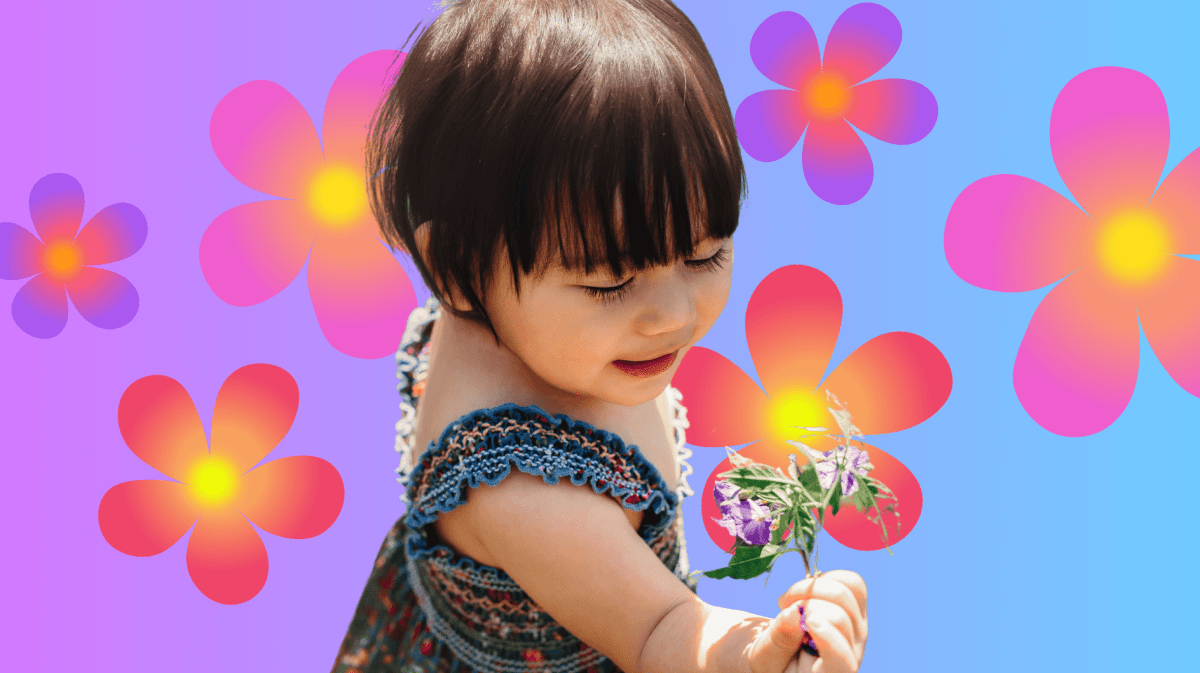 Kleinkind mit Kleid steht auf einer Wiese und hält eine Blume in der Hand.