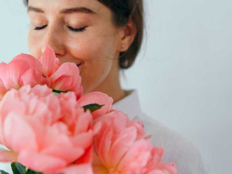 Frau lächelt in einen Strauß Pfingstrosen hinein