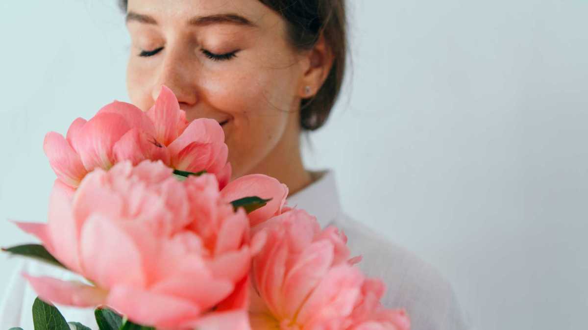 Frau lächelt in einen Strauß Pfingstrosen hinein