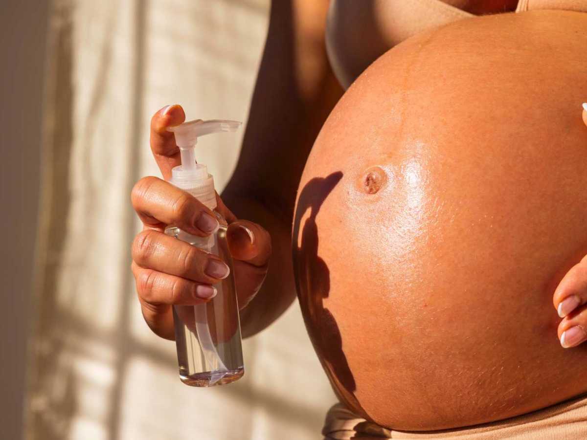 Schwangere Frau cremt ihren Bauch ein.