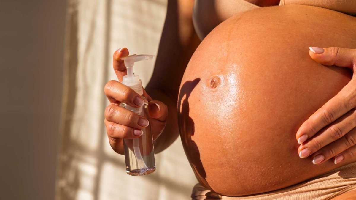 Schwangere Frau cremt ihren Bauch ein.