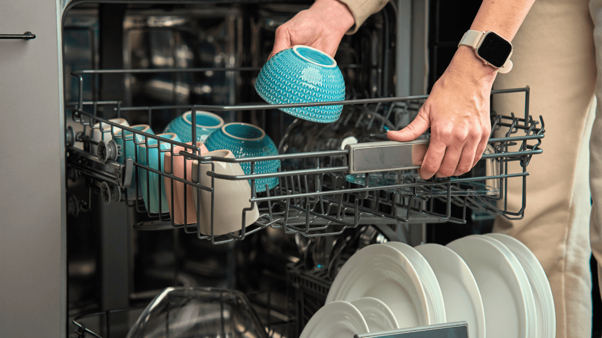 Person räumt Geschirr, eine blaue Schale, in Spülmaschine.