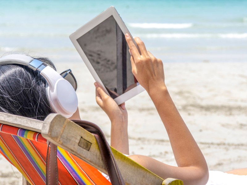 Frau liest mit ihrem eBook-Reader am Strand im Urlaub