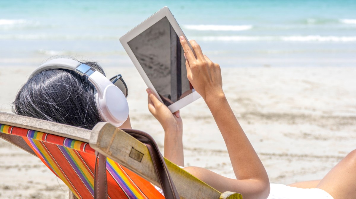 Frau liest mit ihrem eBook-Reader am Strand im Urlaub