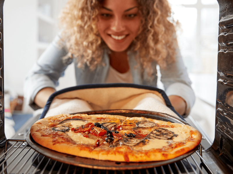 Frau holt Pizza aus Backofen.