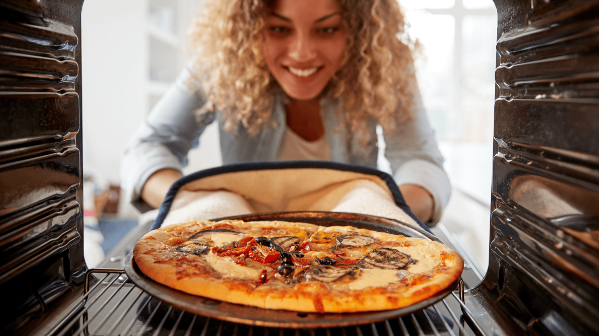 Frau holt Pizza aus Backofen.