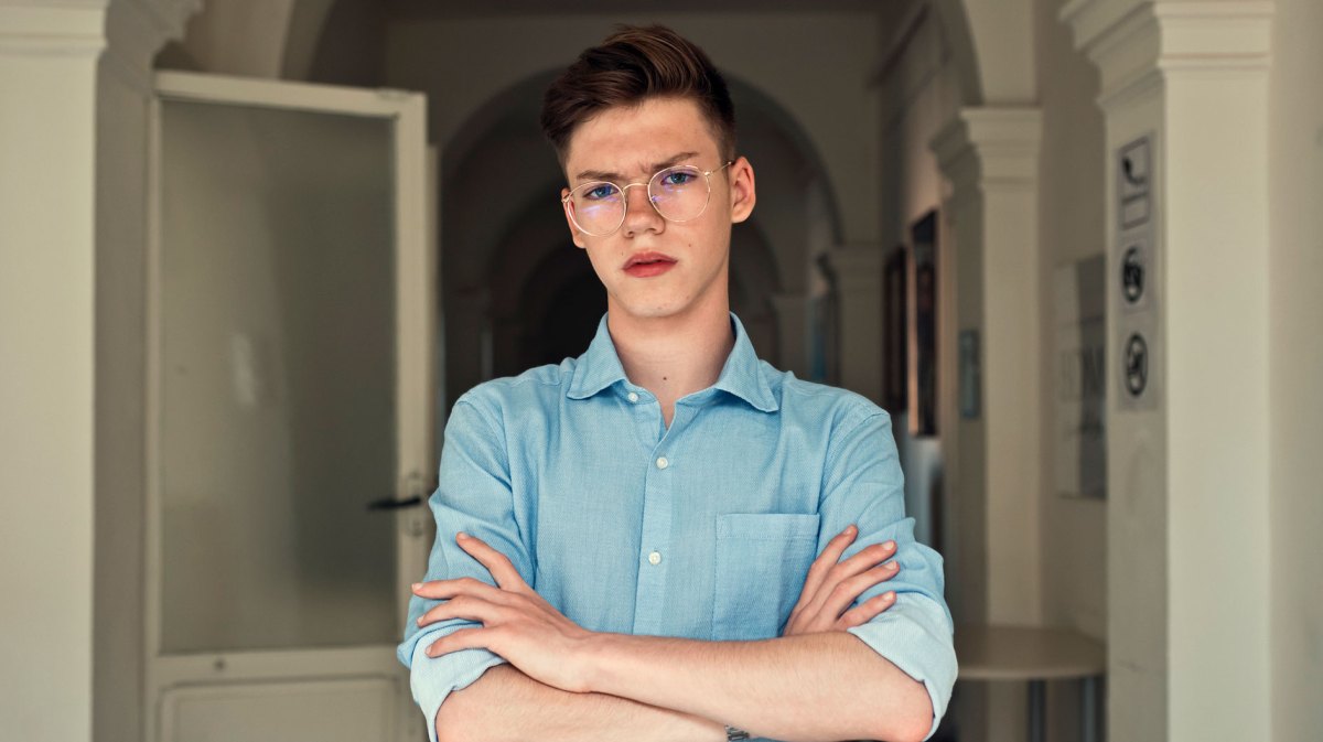 Porträt eines Teenagers, der mit verschränkten Armen und böse Blick im Flur einer Wohnung steht.