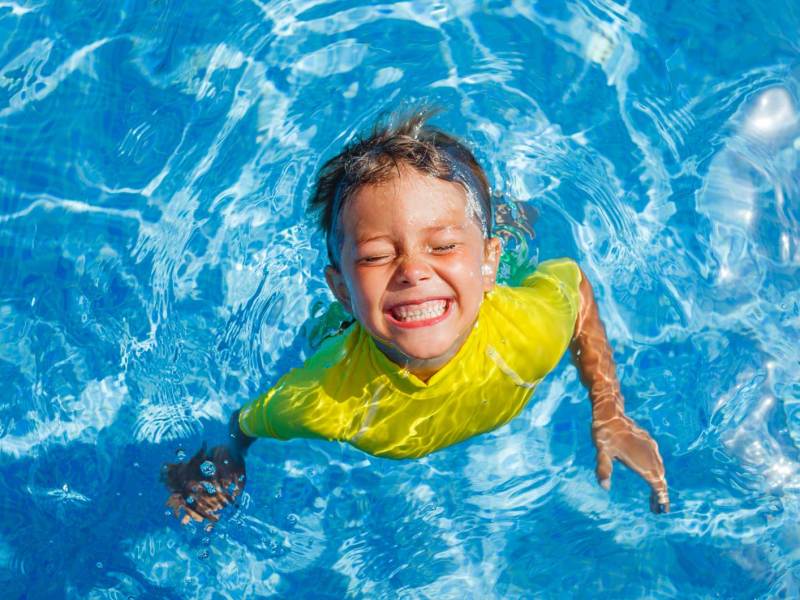 Junge im Pool mit gelbem Schwimmshirt.