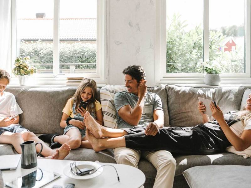 Vierköpfige Familie sitzt auf dem Sofa, alle haben ein digitales Gerät in den Händen.