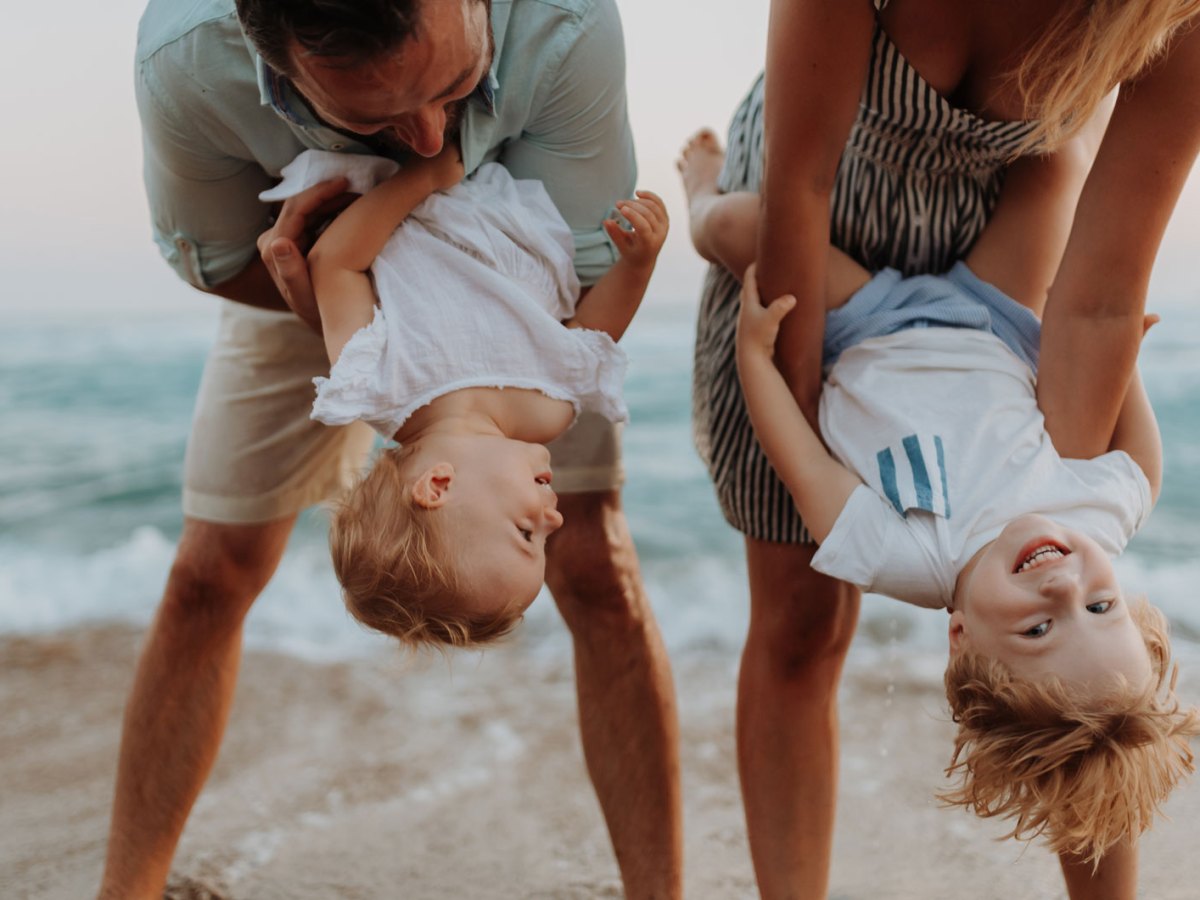 Junge Familie mit zwei kleinen Kindern, die gemeinsam am Strand herumalbern.