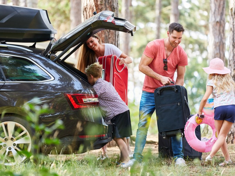 Kinder helfen Eltern beim Koffer tragen aus dem Auto im Wald.