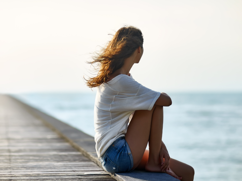 Frau in einem weißen T-Shirt sitzt auf einem Holzsteg am Meer