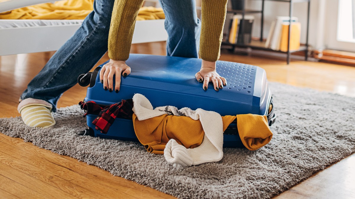 Frau, die versucht ihren vollen Koffer zu schließen.