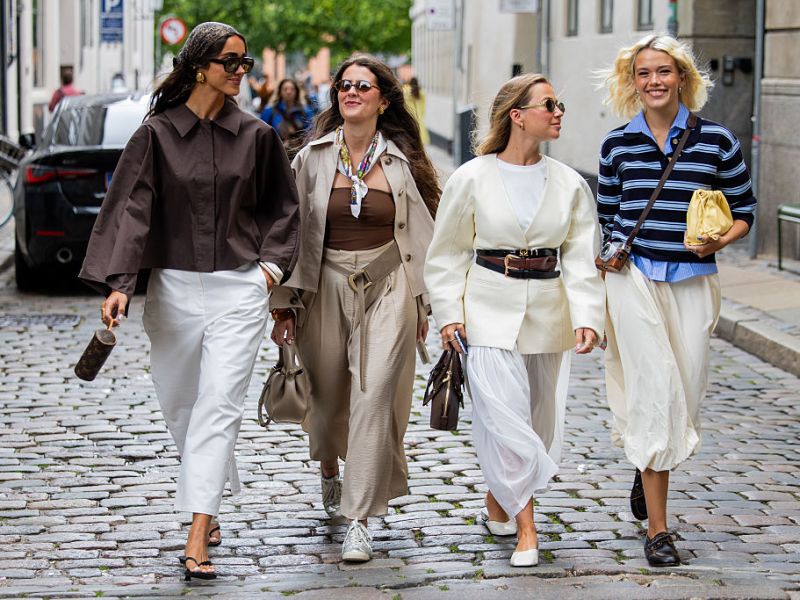 COPENHAGEN, DENMARK - AUGUST 04: A guest wears brown head scarf, brown blouse, white pants & a guest wears beige jacket, pants, brown top & a guest wears creme white jacket, black brown belts, white skirt & a guest wears blue black striped polo shirt, beige skirt outside Forza Collective during Copenhagen Fashion Week day one on August 04, 2025 in Copenhagen, Denmark.