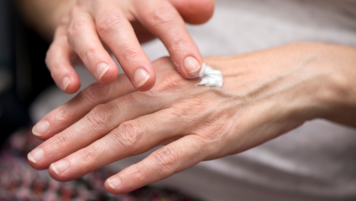 Frau cremt ihre Hände mit Handcreme ein.