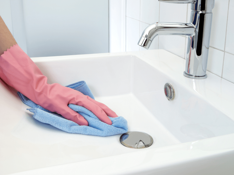 Frau, die das Waschbecken im Bad putzt.