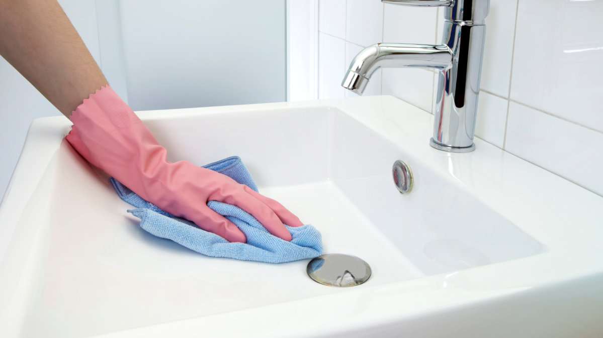 Frau, die das Waschbecken im Bad putzt.