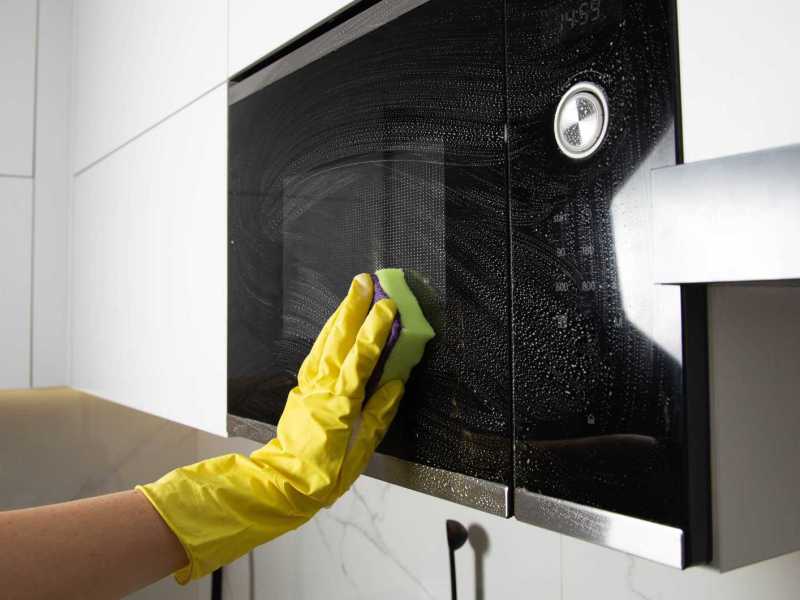 Mikrowelle wird von einer Hand im gelben Handschuh geputzt