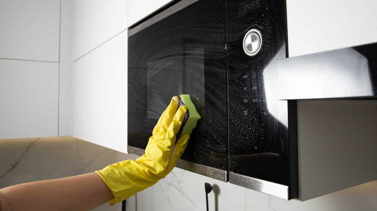 Mikrowelle wird von einer Hand im gelben Handschuh geputzt