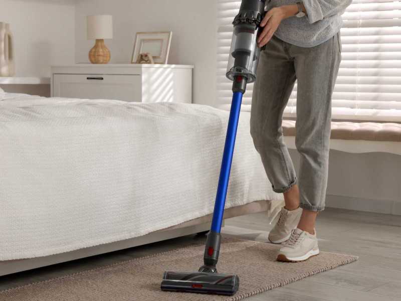 Frau saugt mit einem Staubsauger ihr Schlafzimmer