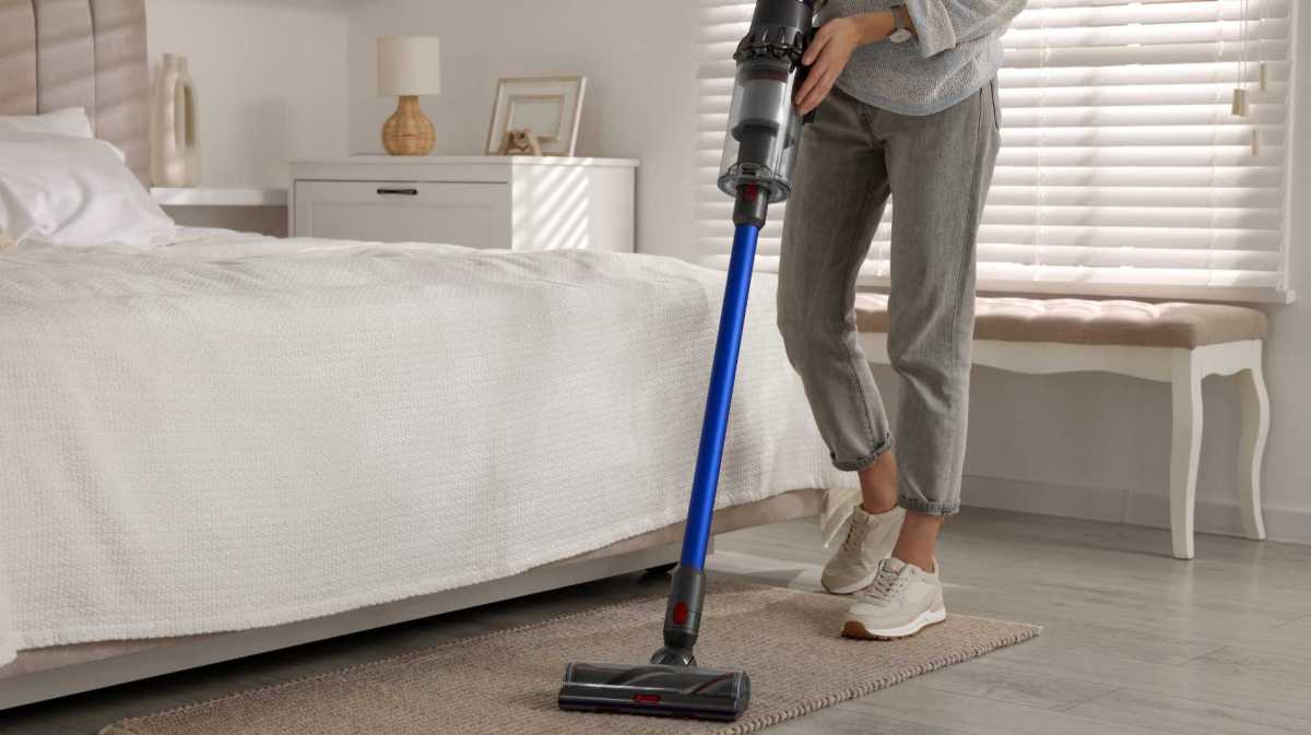 Frau saugt mit einem Staubsauger ihr Schlafzimmer