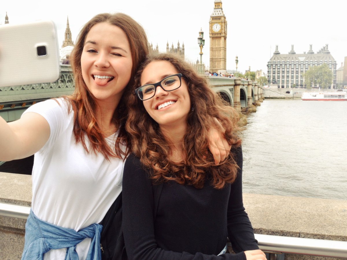 Zwei Teenager-M&auml;dchen stehen in London an der Themse und machen ein Selfie mit Big Ben im Hintergrund.