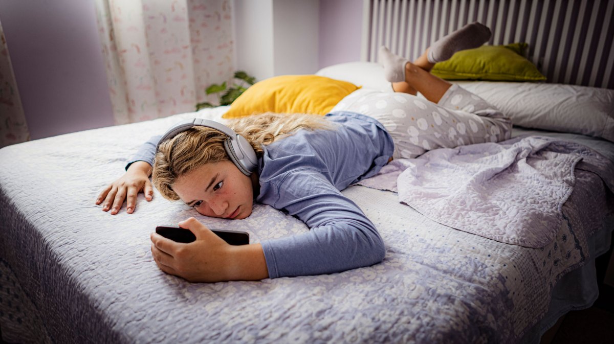 Mädchen im Teenageralter, liegt mit ihrem Handy und Kopfhörern faul auf ihrem Bett.