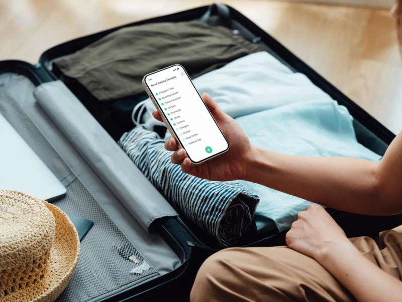 Frau packt Koffer mit einer Packliste auf ihrem Smartphone.