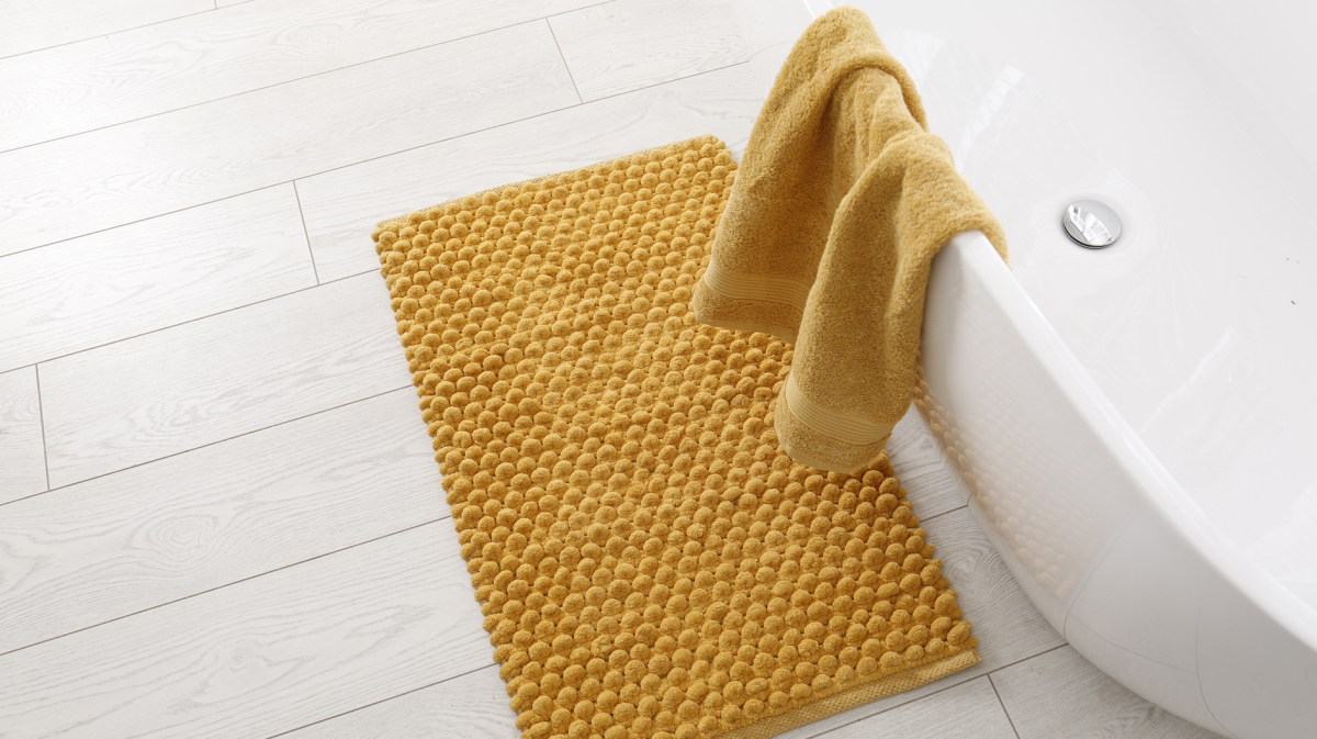 Gelbe Badematte liegt vor Badewanne