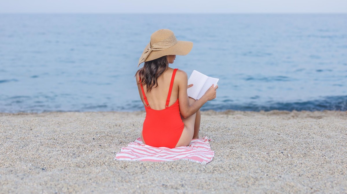 Frau in rotem Badeanzug liest Buch am Strand