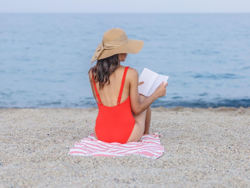 Frau in rotem Badeanzug liest Buch am Strand