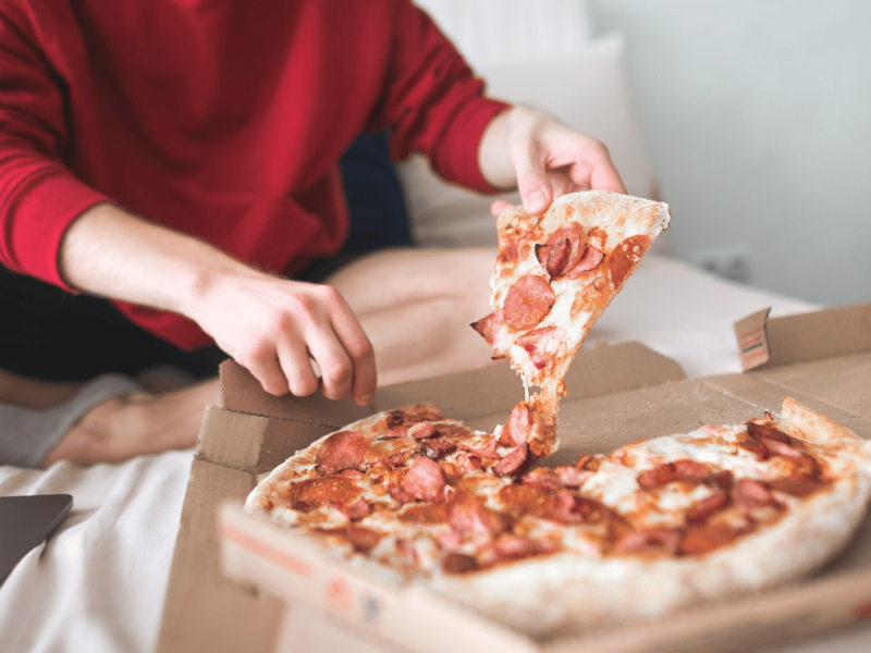 Person isst Pizza auf Bett.