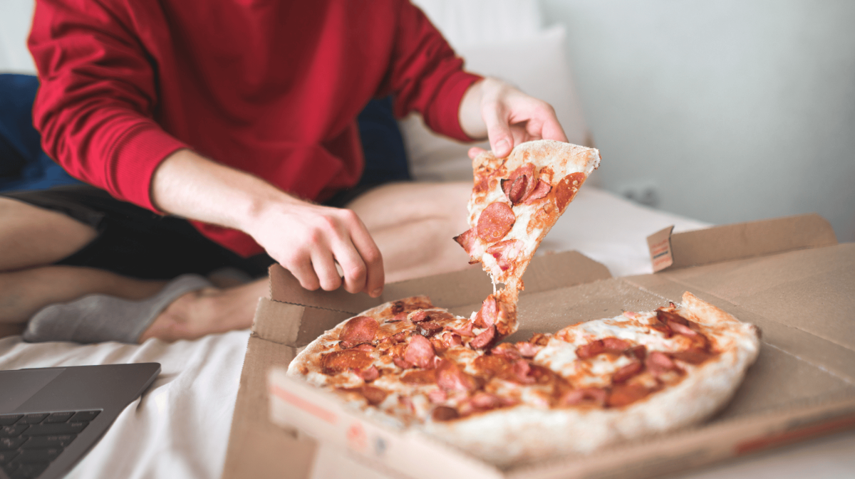 Person isst Pizza auf Bett.