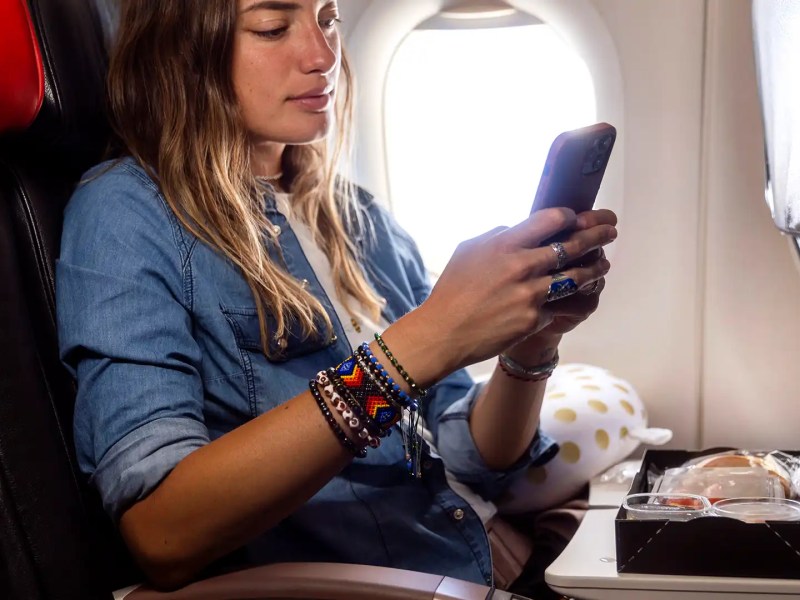 Frau sitzt im Flugzeug mit Essen vor sich und hat Handy in der Hand